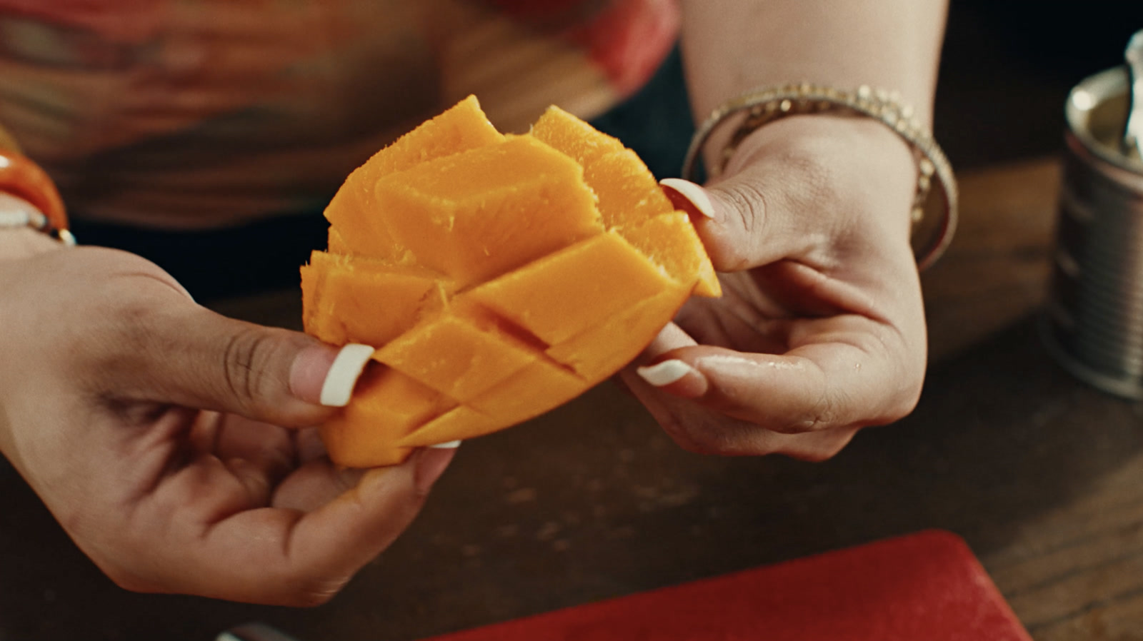 Hands turning a scored mango, bangles and white nails